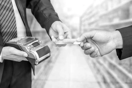 Mano que entrega billetes a un comerciante junto a una terminal de pago con tarjeta sobre un mostrador.